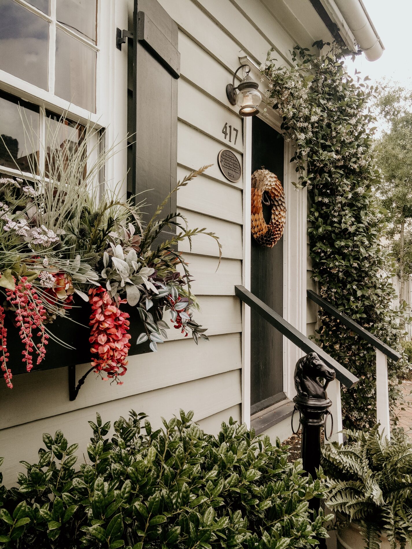 historical-home-property-georgia Front porch of a house with beige siding, black shutters, greenery, and a floral window box beside the door.