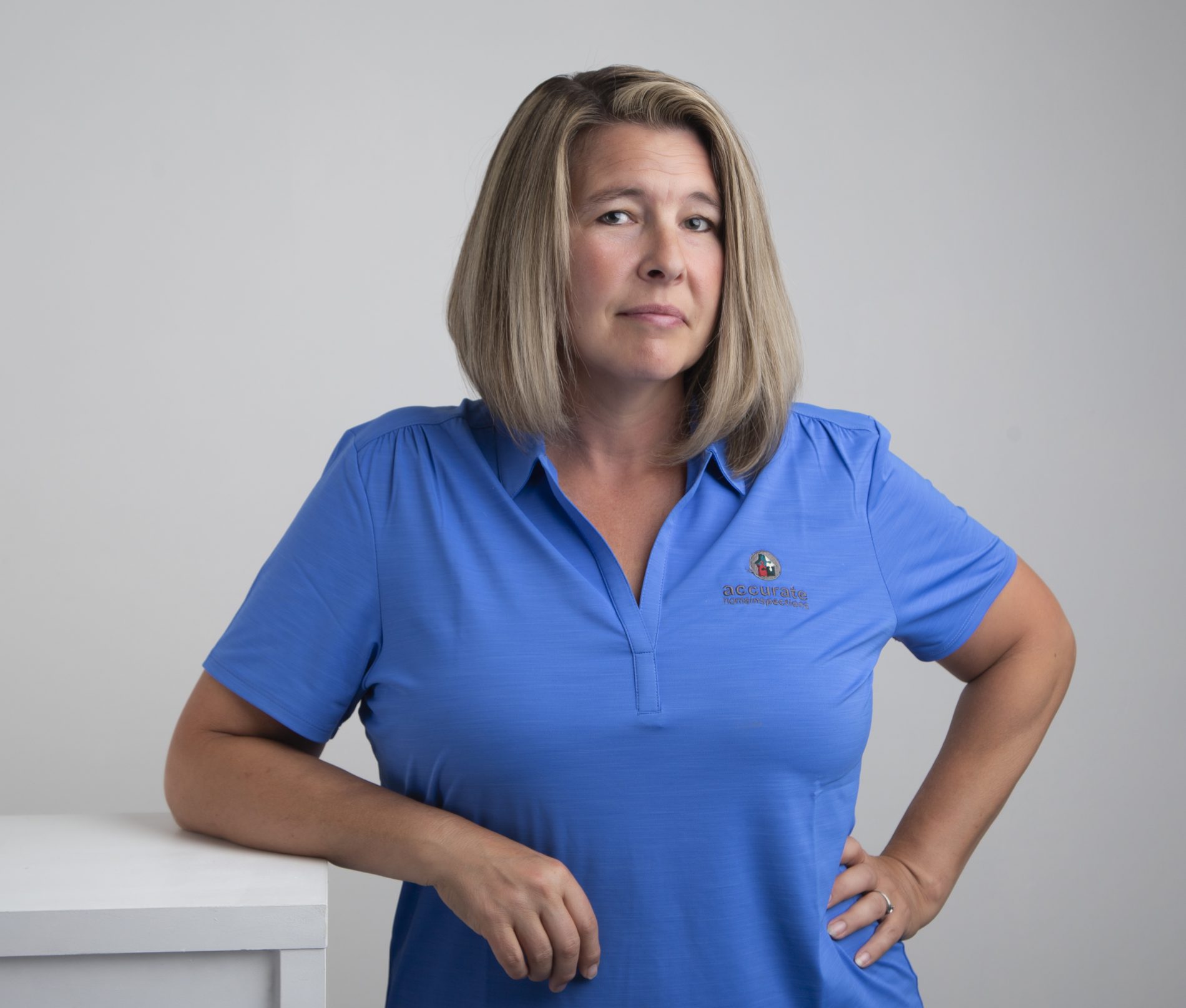Terra Snyder Woman with shoulder-length blonde hair in a blue polo shirt stands with one hand on her hip against a plain background.