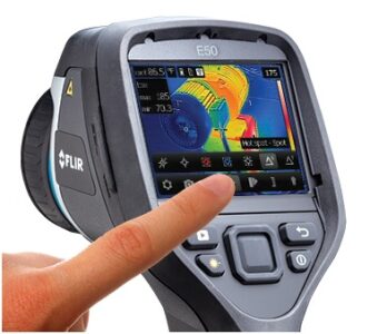 Thermal Imaging cameras detect temperature differential. Different colors correspond to different temperatures, so an inspector is able to identify areas that are abnormally hot or cold. A hand operates a FLIR E50 thermal imaging camera showing a heat map on its display screen.